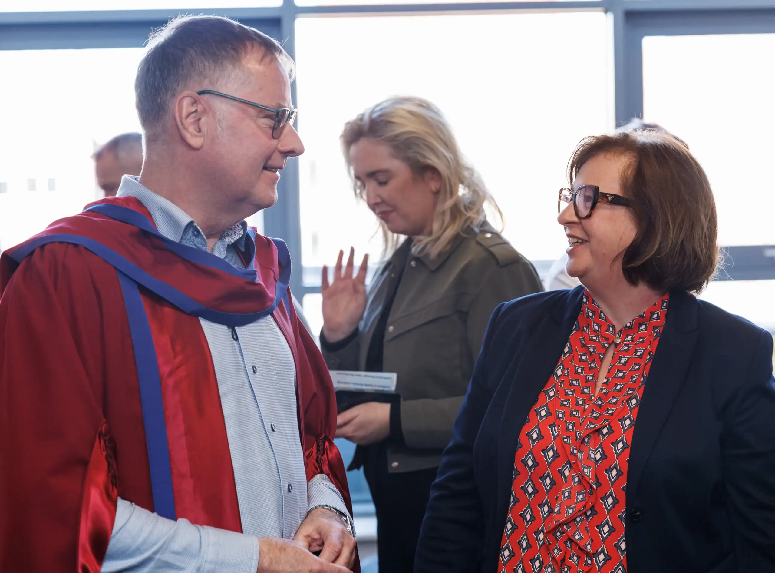 Two people conversing, academic attire present.